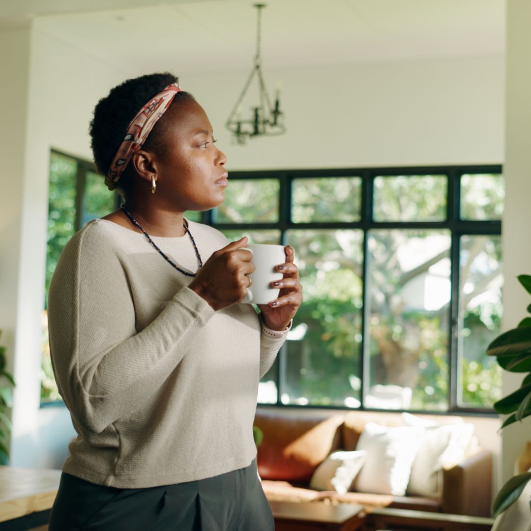 Woman sitting quietly with a cup of tea, looking thoughtful, representing food noise and persistent thoughts about food in PMOS.